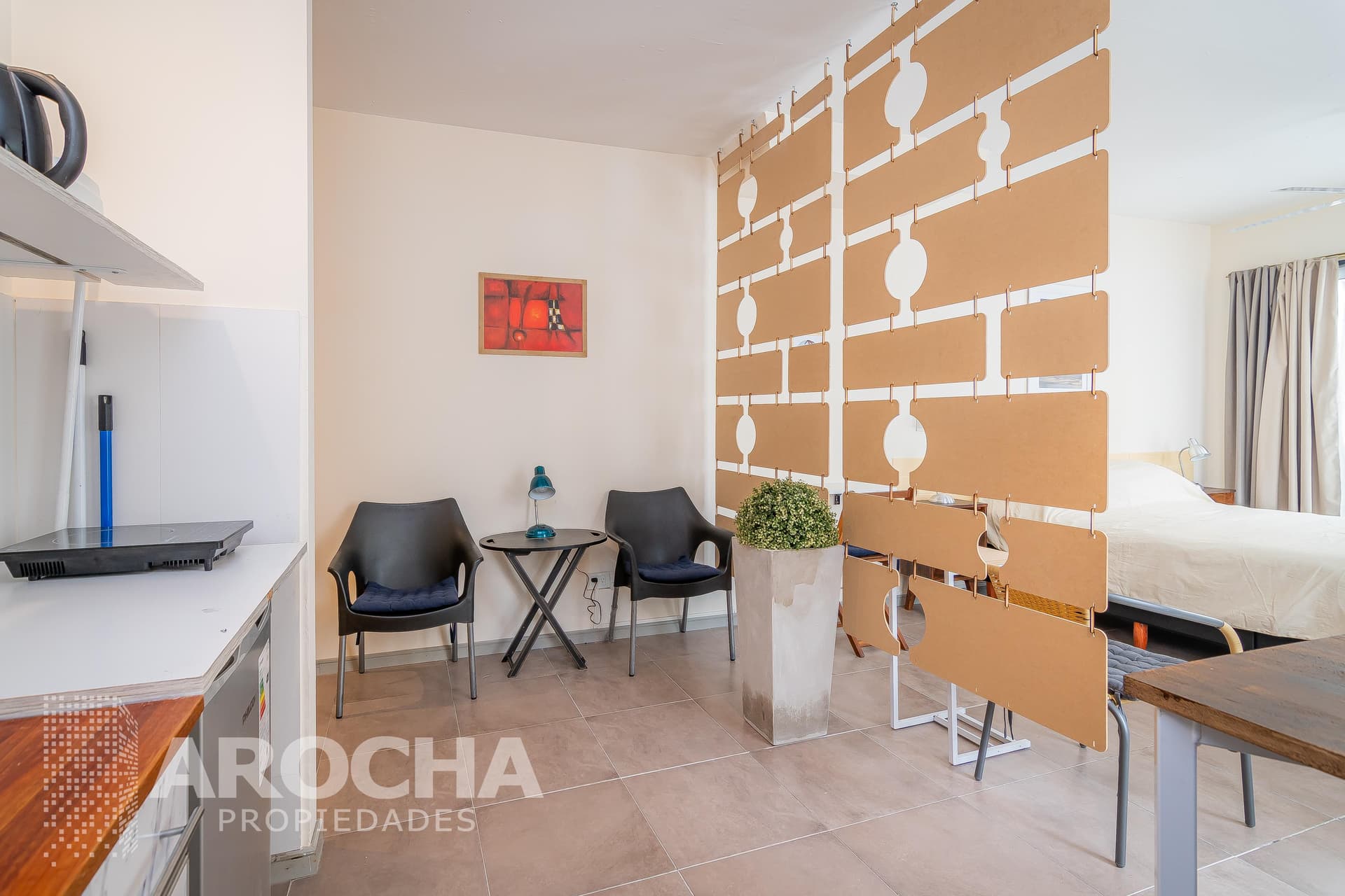Living con cocina integrada, separador de ambientes y mesa con sillas.
