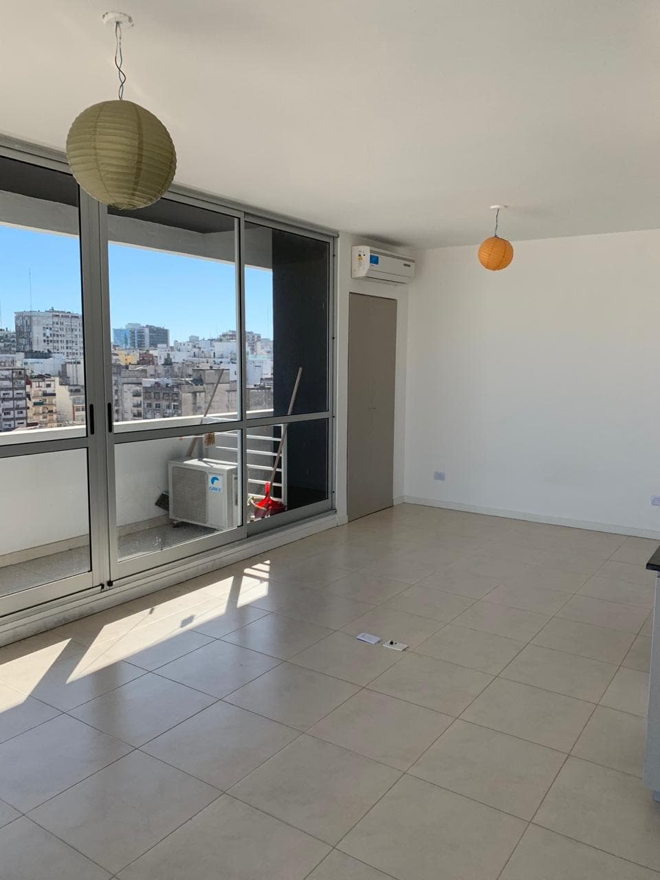 Living vacío con ventanal al balcón, unidad de aire y vista.