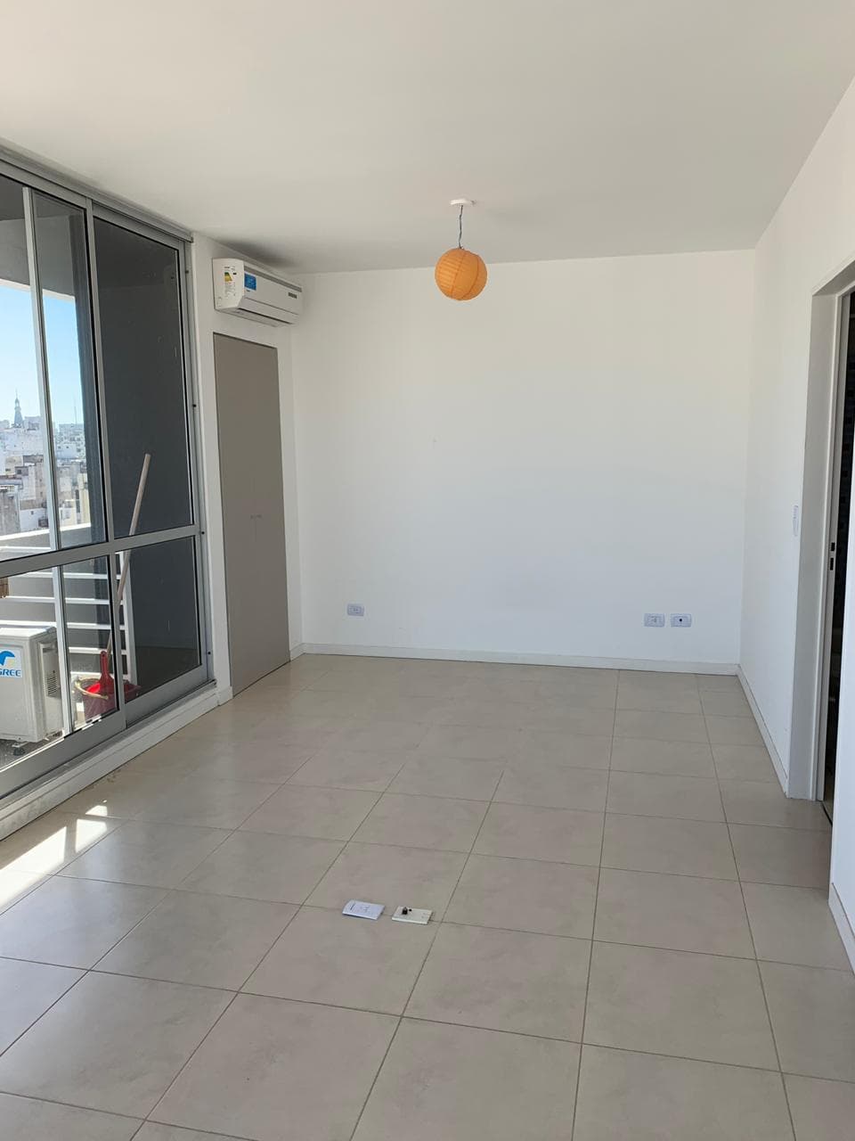 Living vacío con paredes blancas, piso de baldosas y puerta.