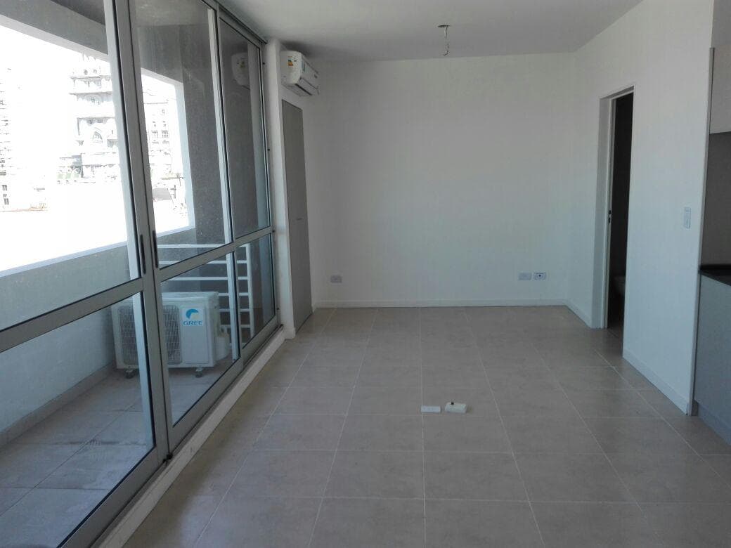 Living vacío con ventanal, balcón, aire acondicionado y puerta.