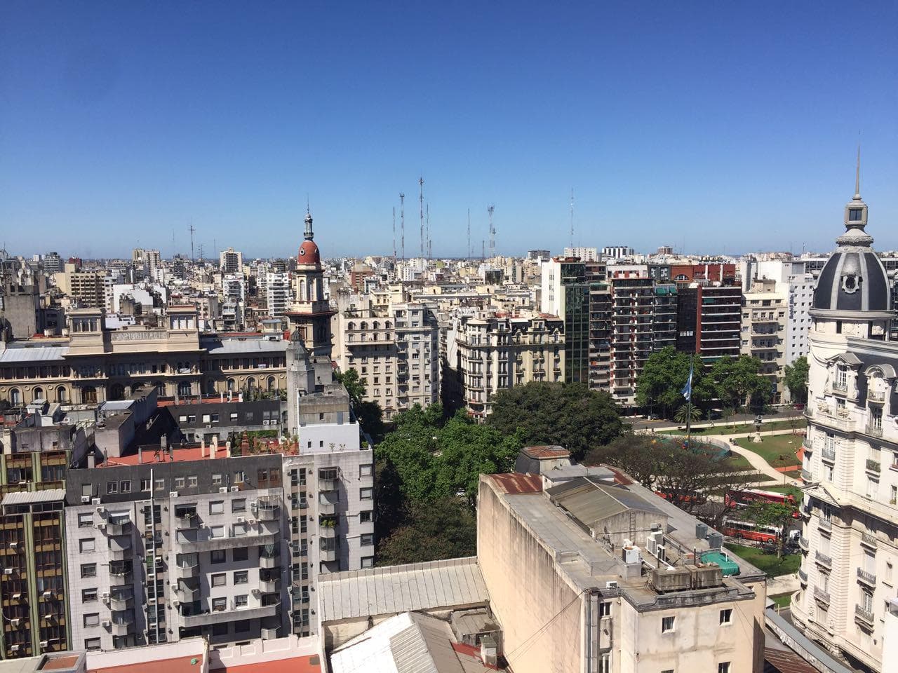 Vista aérea de la ciudad con edificios, una plaza y cielo azul claro.
