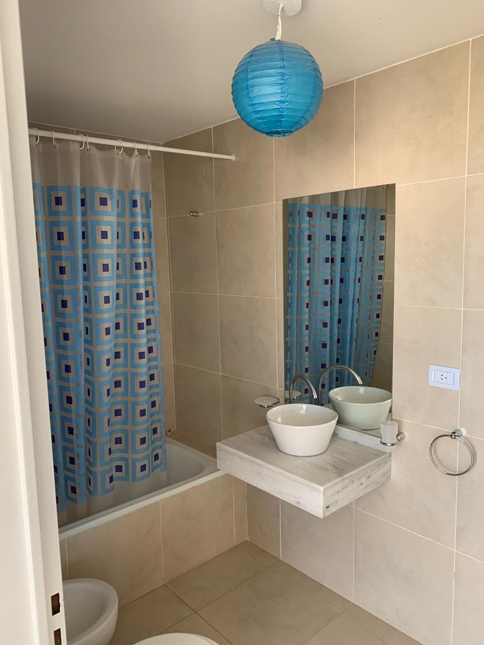Baño con bañera con cortina, lavatorio con bacha y espejo.