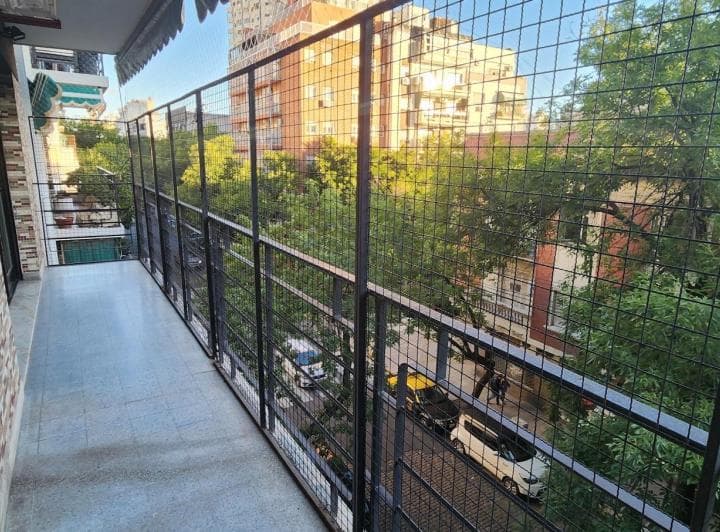 Balcón largo con rejas de seguridad y vista arbolada a la calle.