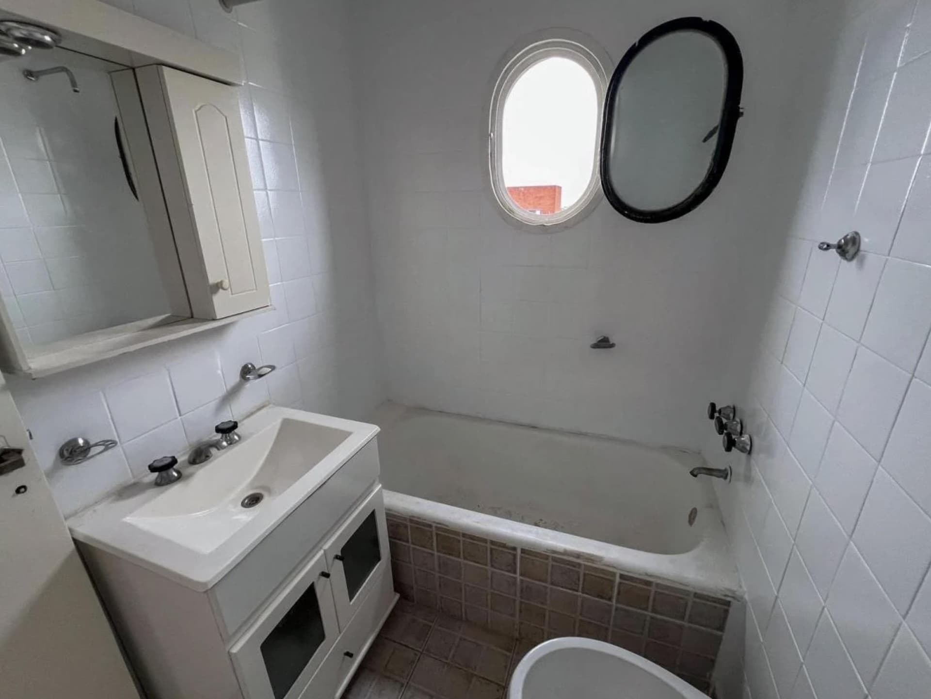 Baño con bañera, ventana ovalada, bacha y espejo botiquín