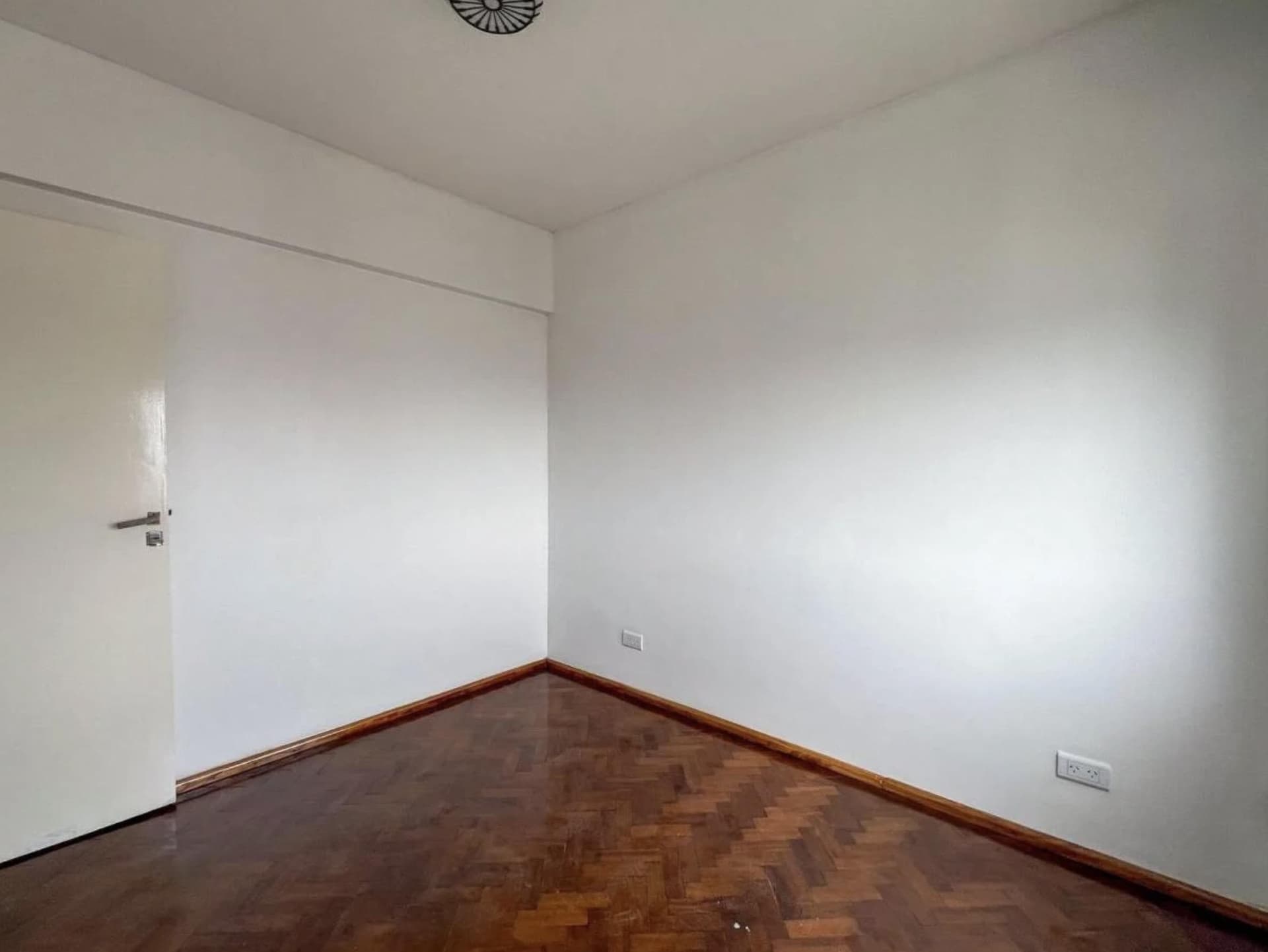 Dormitorio vacío con piso de parquet y paredes blancas