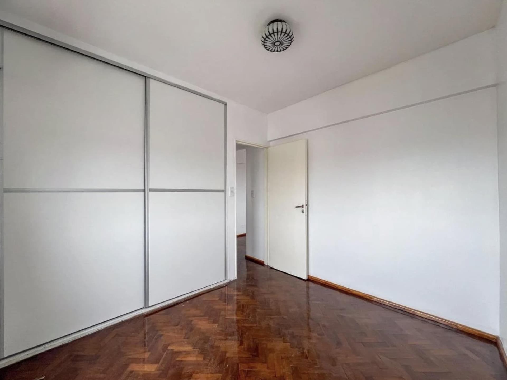 Dormitorio vacío con placard de puertas corredizas y piso de parquet