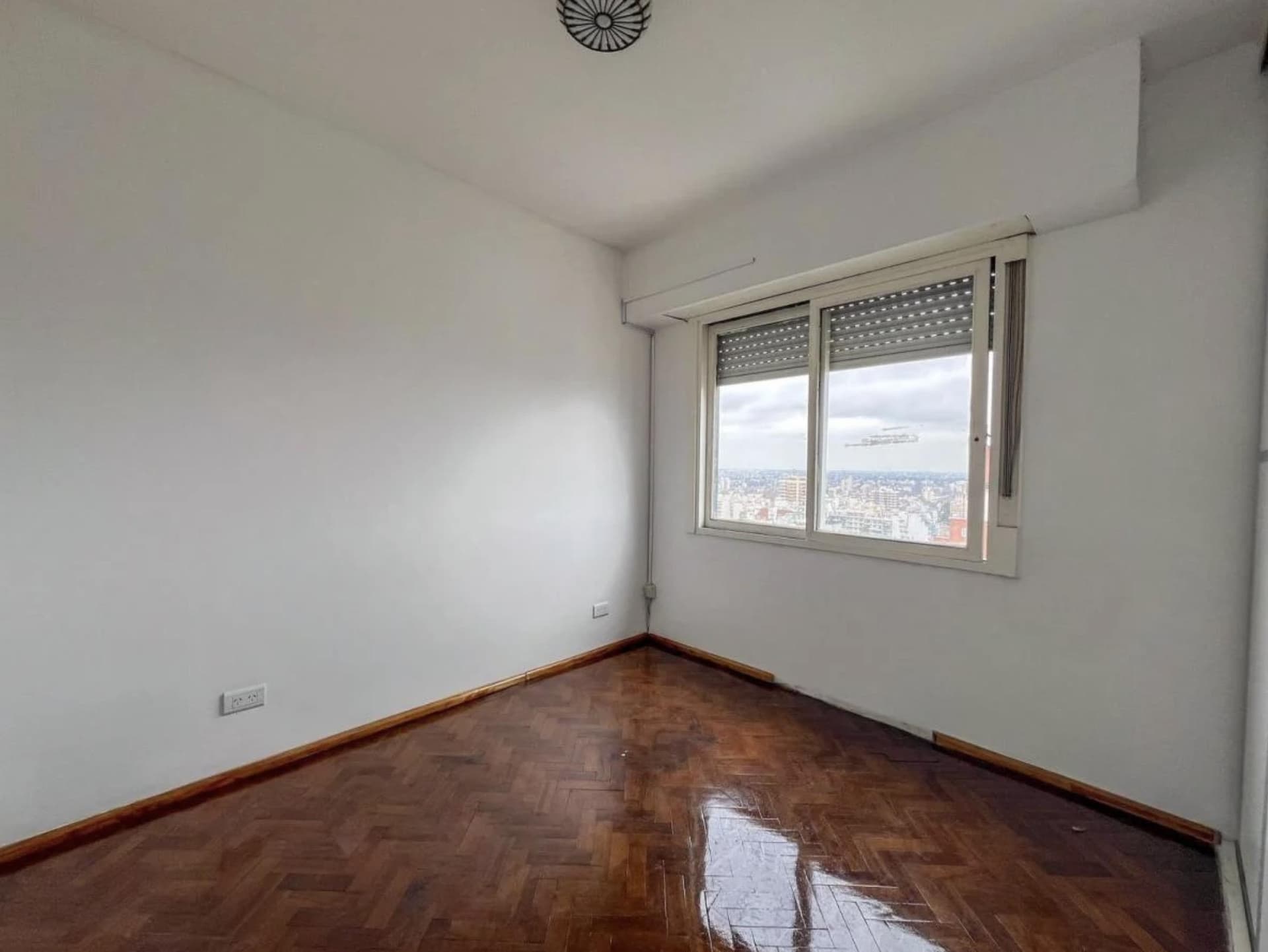 Dormitorio vacío con ventana y persiana, piso de parquet