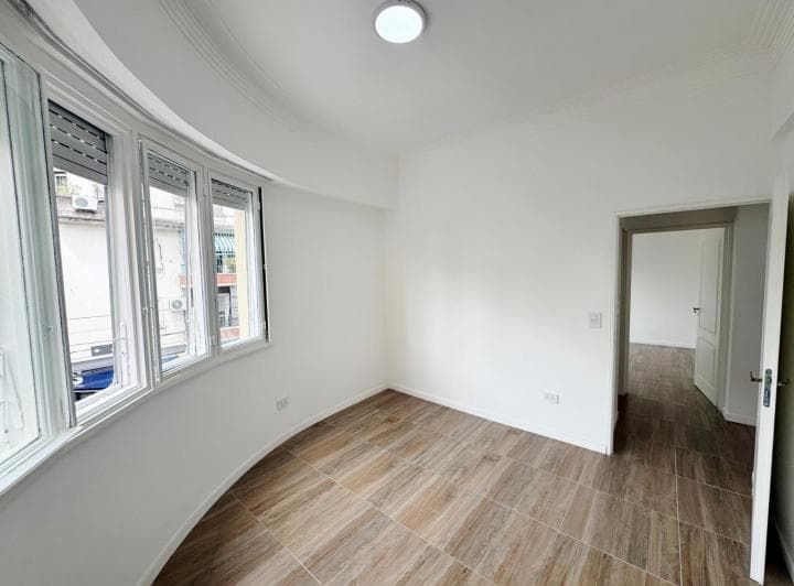 Dormitorio vacío con ventana curva, pisos cerámicos y acceso a otra habitación.