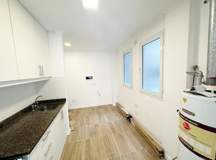 Cocina con mesada, bacha, alacenas, termotanque y ventanas laterales.
