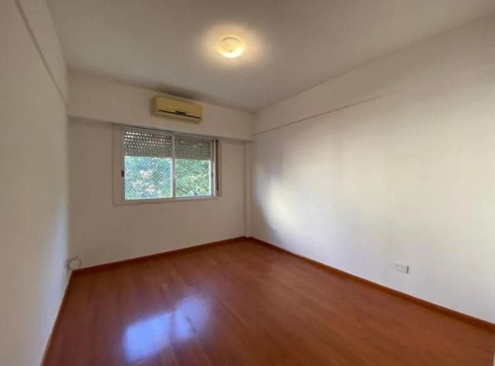 Dormitorio vacío con piso de madera, paredes blancas y ventana con persiana.
