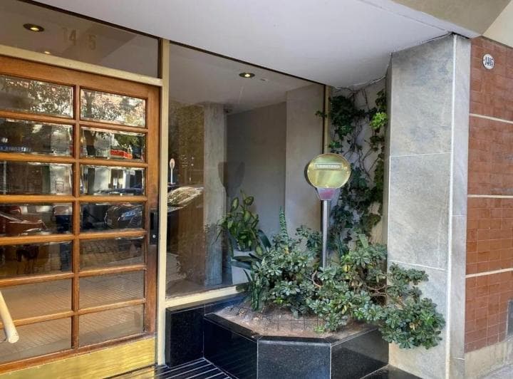 Fachada del edificio con puerta de entrada de madera y vidrio, y plantas decorativas.