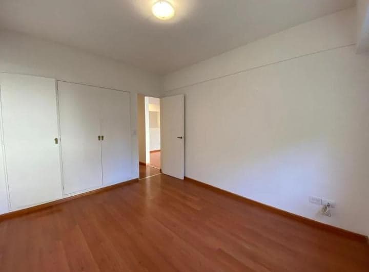 Dormitorio vacío con piso de madera, paredes blancas y placard empotrado blanco.