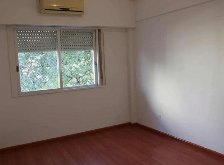 Dormitorio vacío con piso de madera, paredes blancas y ventana con persiana.