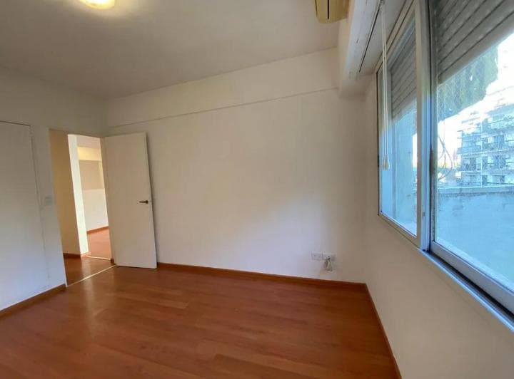 Dormitorio vacío con piso de madera, paredes blancas y ventana con persiana.