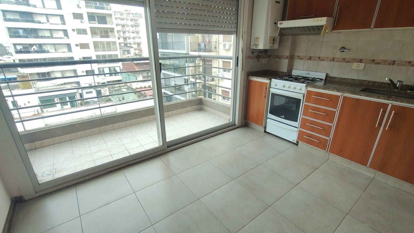 Cocina integrada con anafe, bacha, mesada y alacenas, junto a balcón.