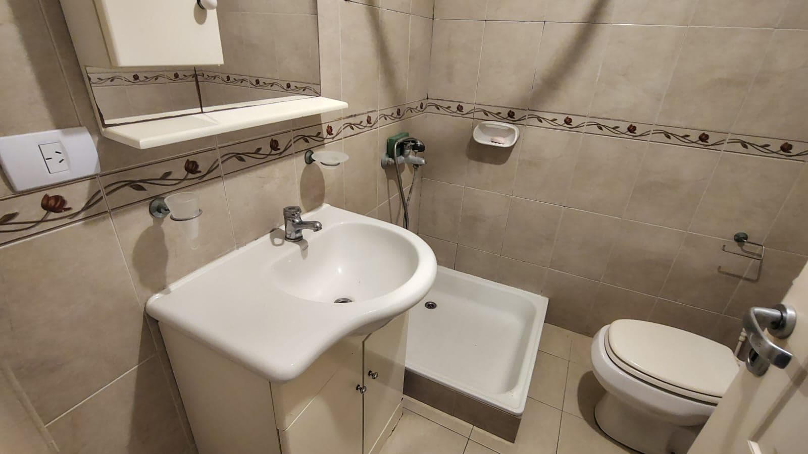 Baño con ducha, vanitory, inodoro y azulejos decorados con guarda floral.