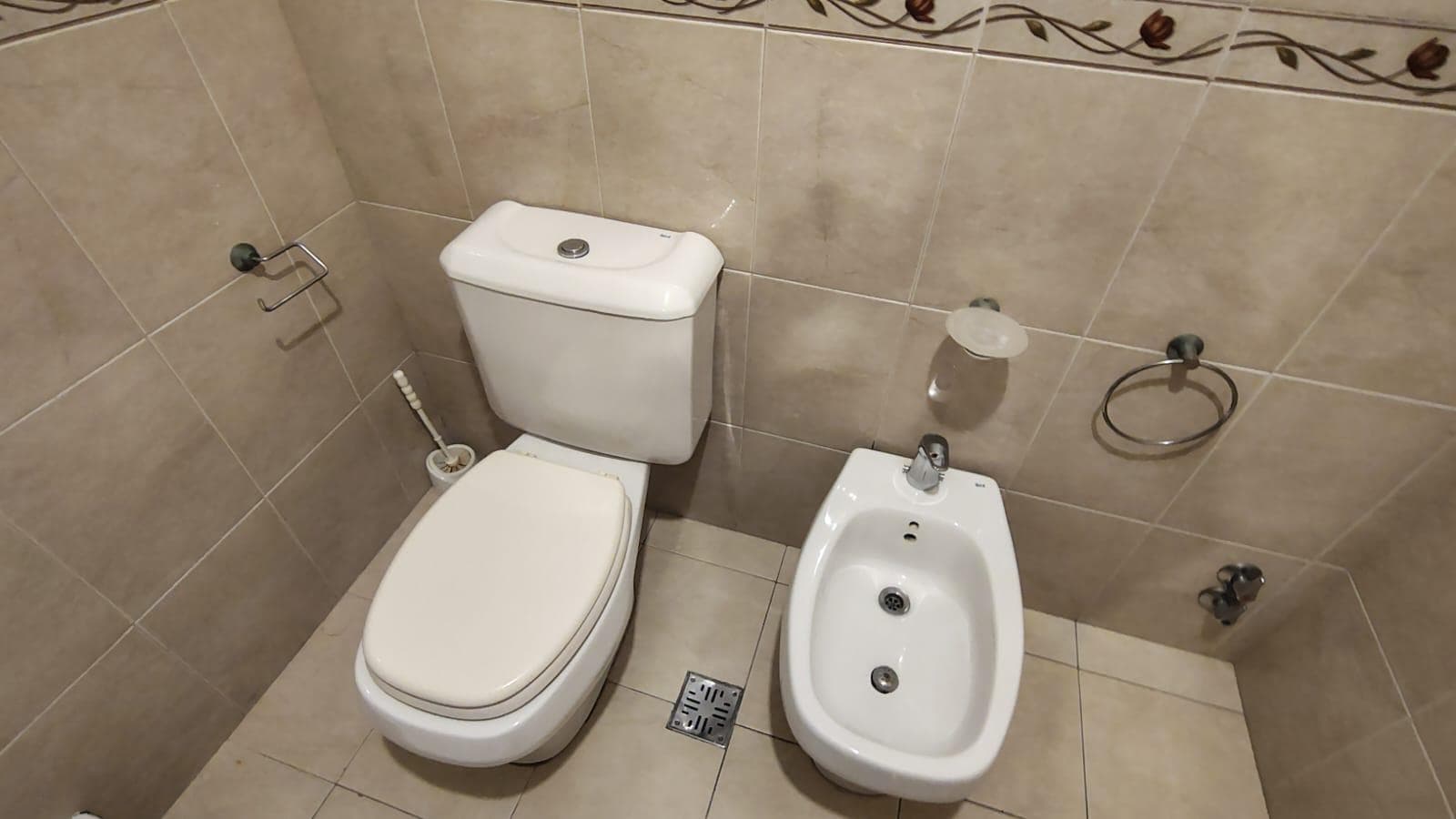 Baño con inodoro, bidet y azulejos con guarda decorativa en la pared.