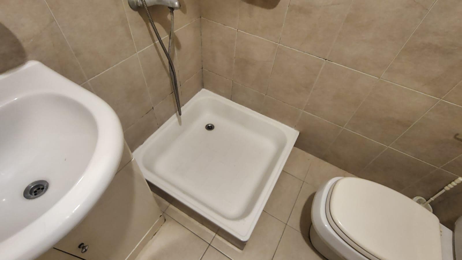 Baño con ducha, inodoro y vanitory, con azulejos beige y guarda.