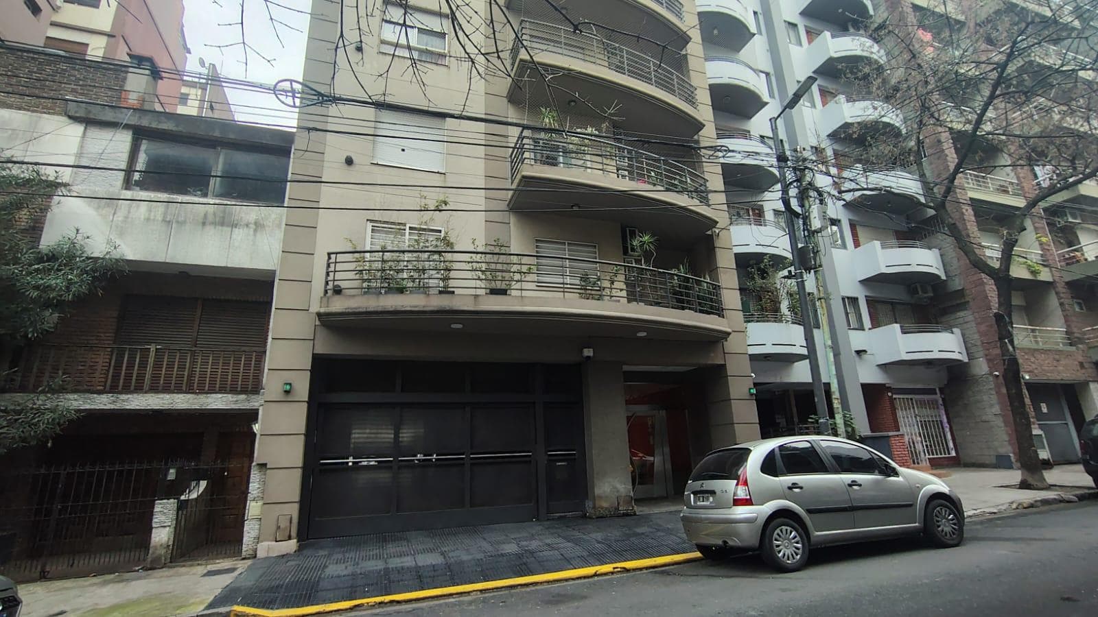 Fachada del edificio con entrada de cochera, balcones y árboles.