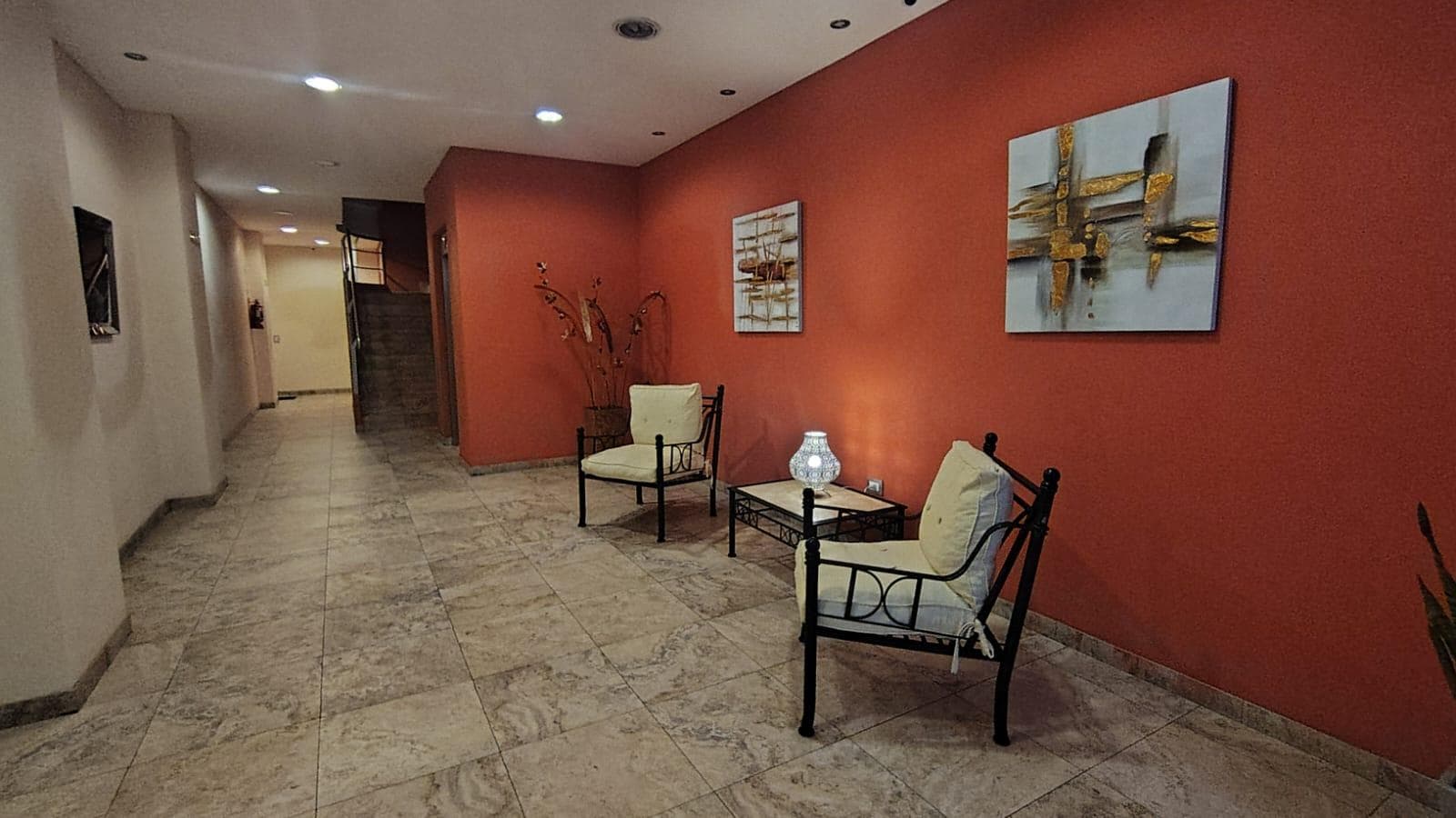 Hall de entrada del edificio con sillones, pared roja y pasillo largo.