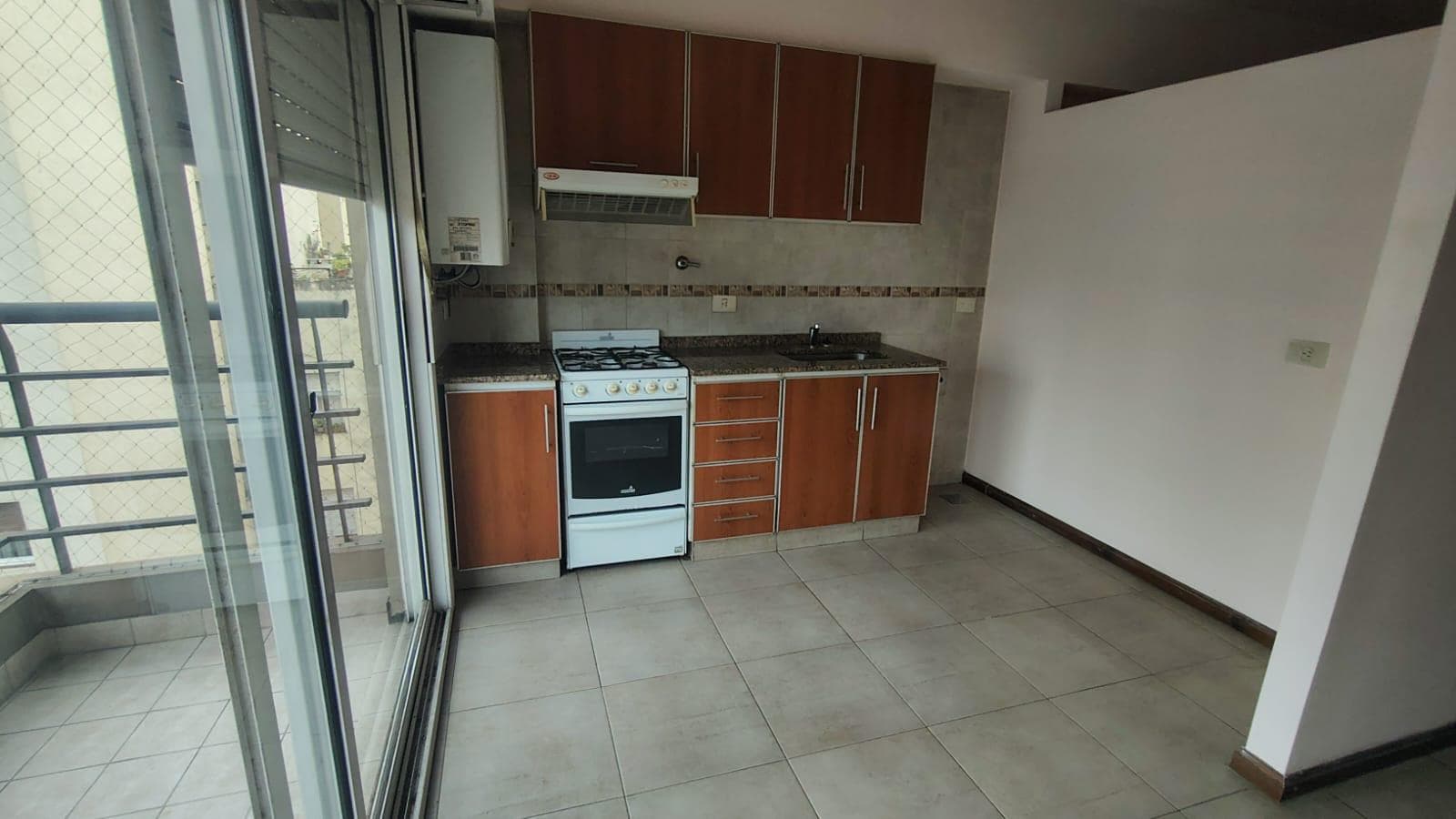 Cocina integrada con anafe, bacha y alacenas de madera, junto a balcón.