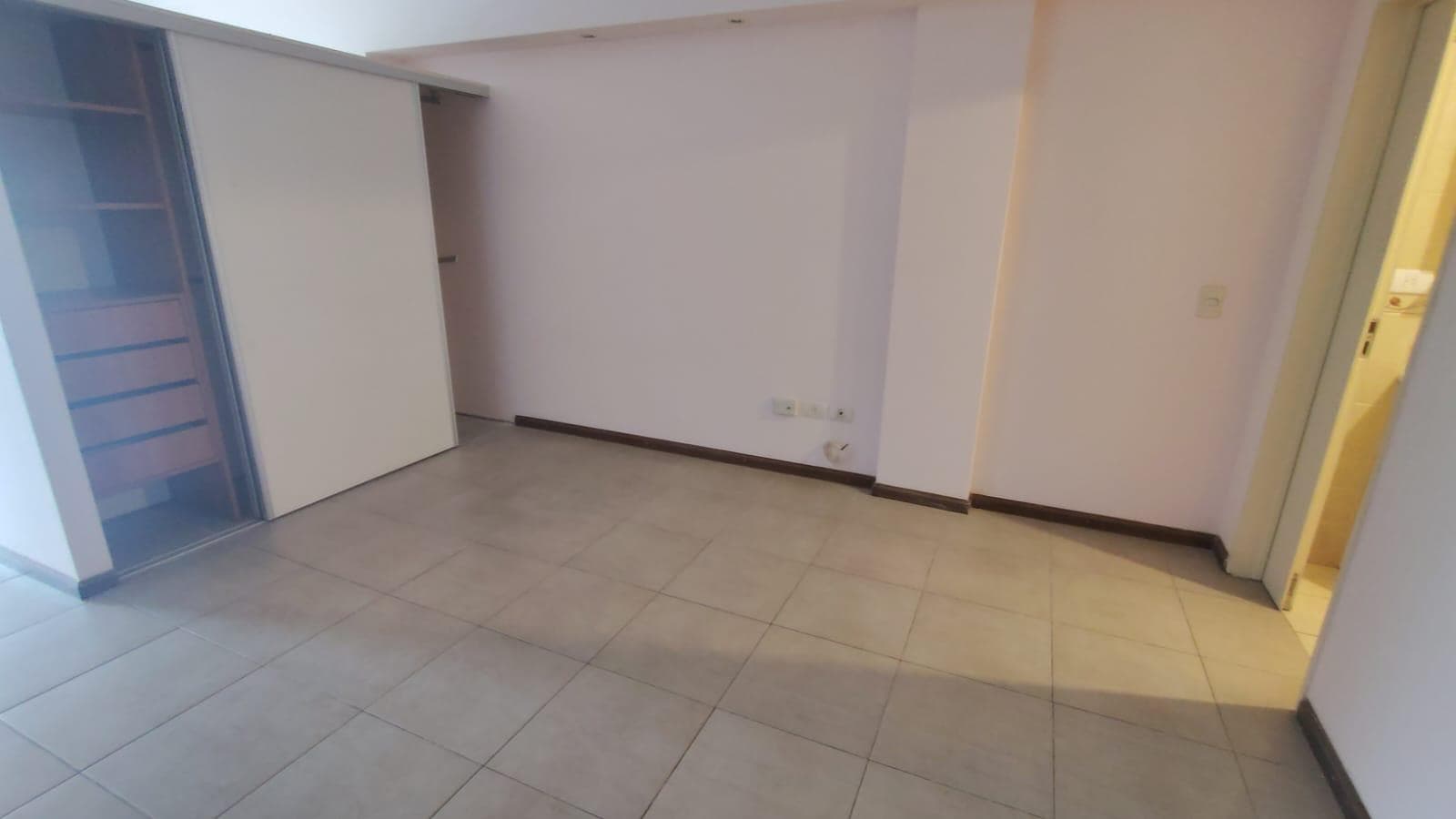 Living vacío con placard de puertas corredizas y piso de baldosas claras.