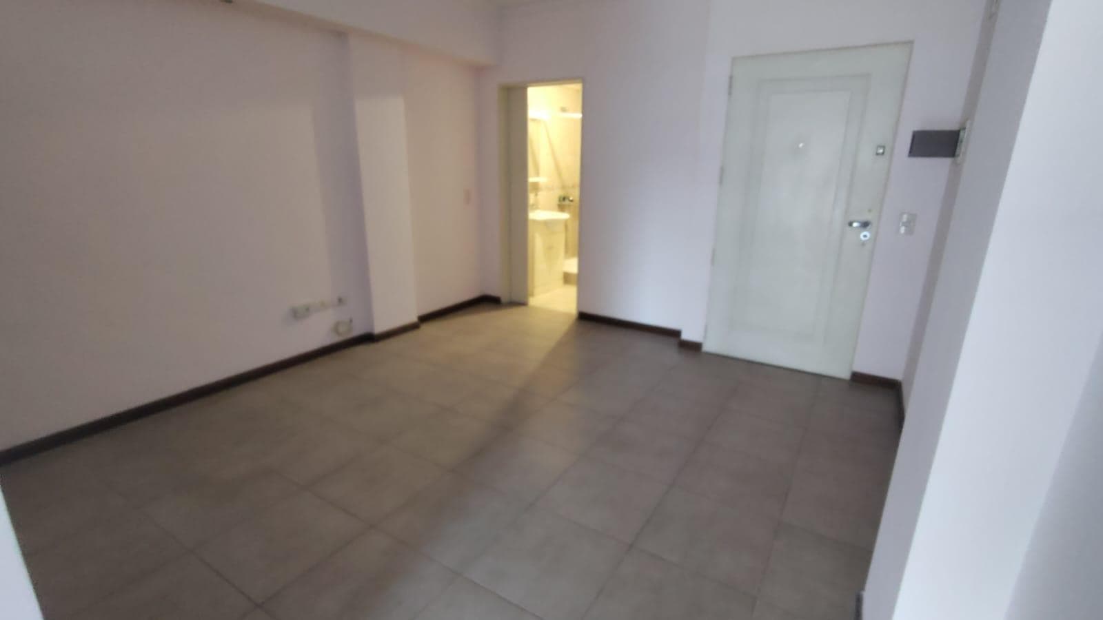 Living vacío con puerta de entrada y se vislumbra el baño al fondo.