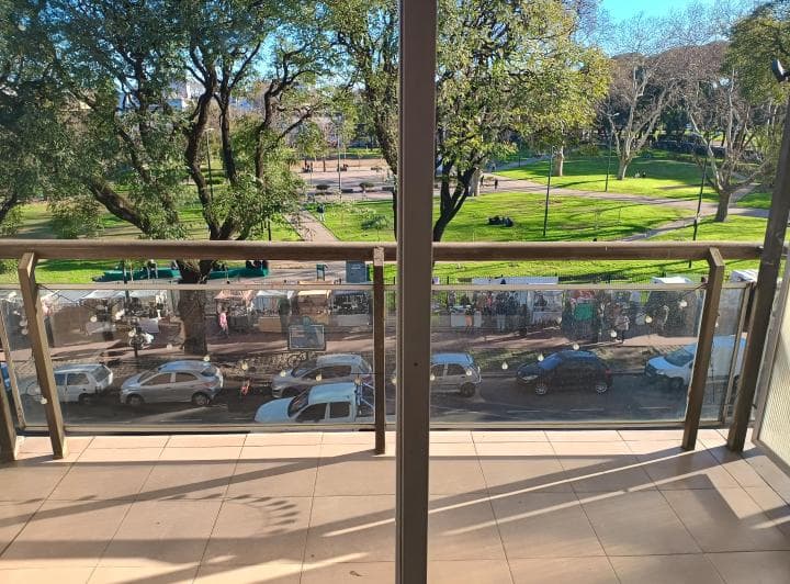 Vista desde balcón a un parque con árboles, personas y calle.