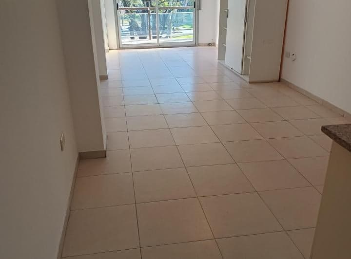 Ambiente principal vacío con piso cerámico y puerta balcón al fondo.