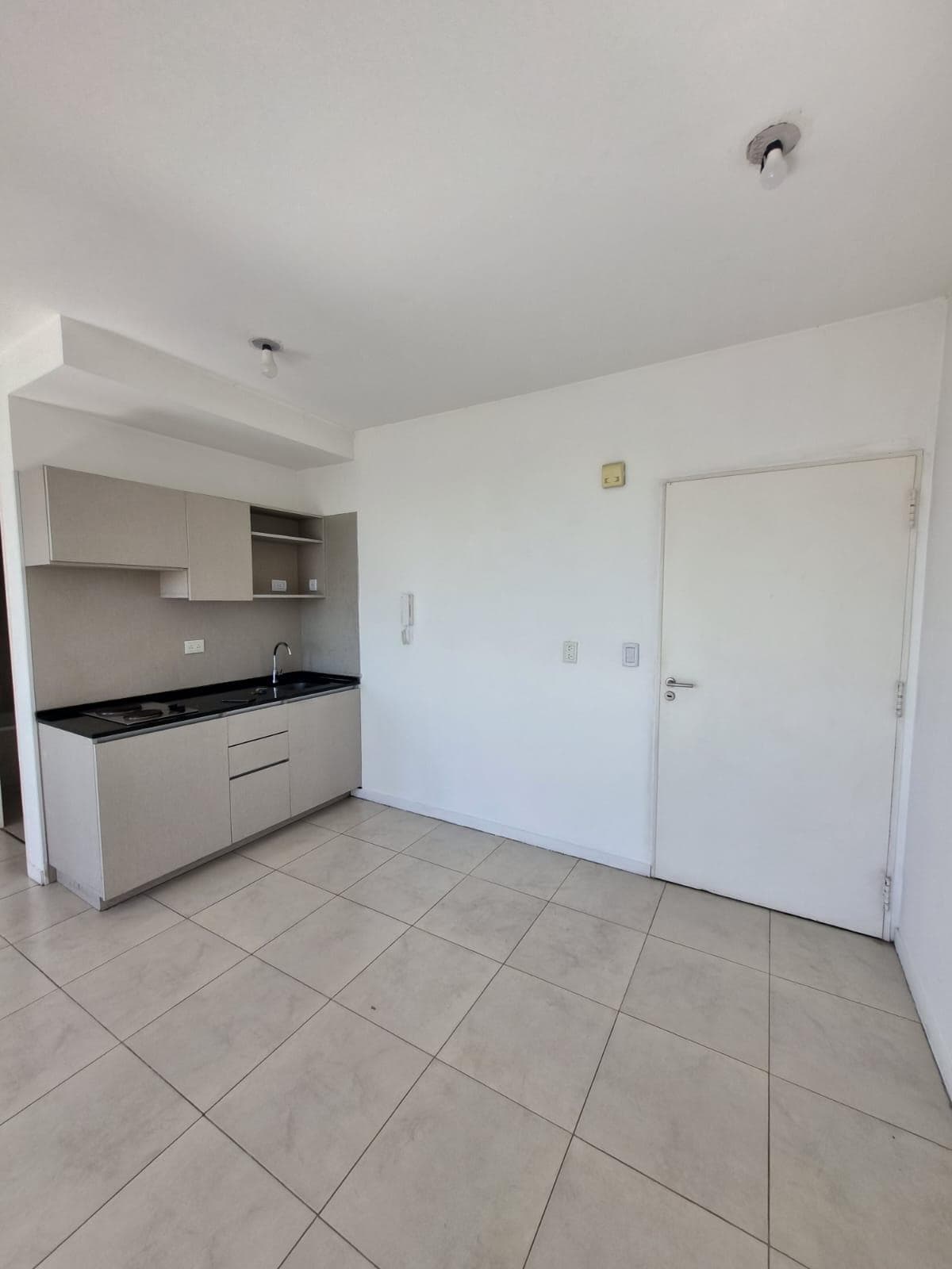 Cocina integrada con mesada oscura, bacha y anafe.