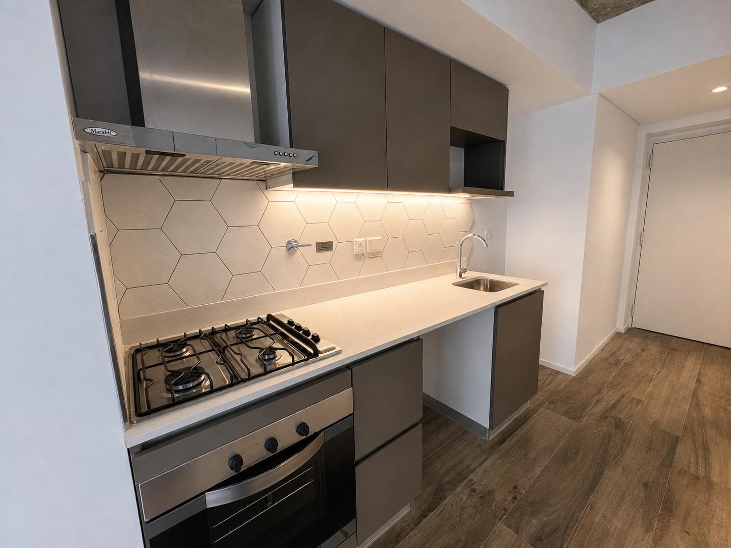 Cocina integrada con anafe a gas, horno, mesada, bacha y alacenas en tono gris.