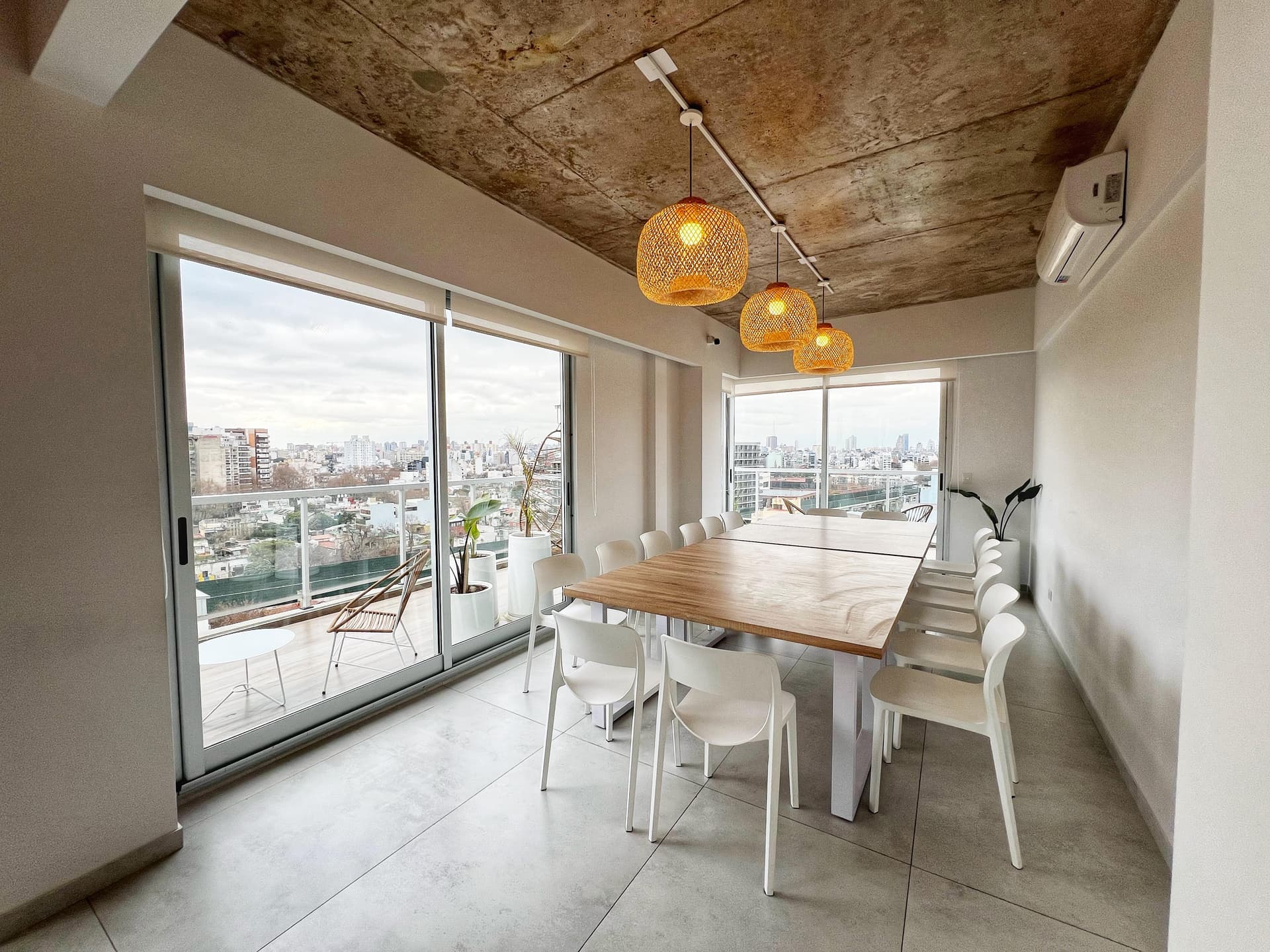 Comedor del SUM con mesa grande de madera, sillas blancas y salida a una terraza.