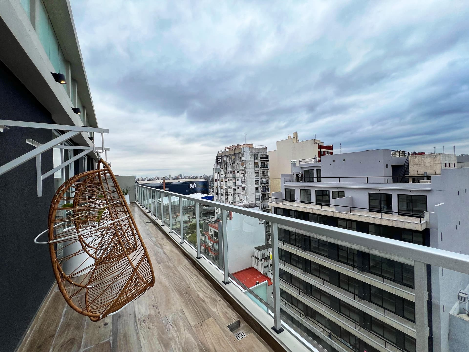 Terraza del edificio con sillas colgantes y baranda de vidrio, ofreciendo vistas de la ciudad.
