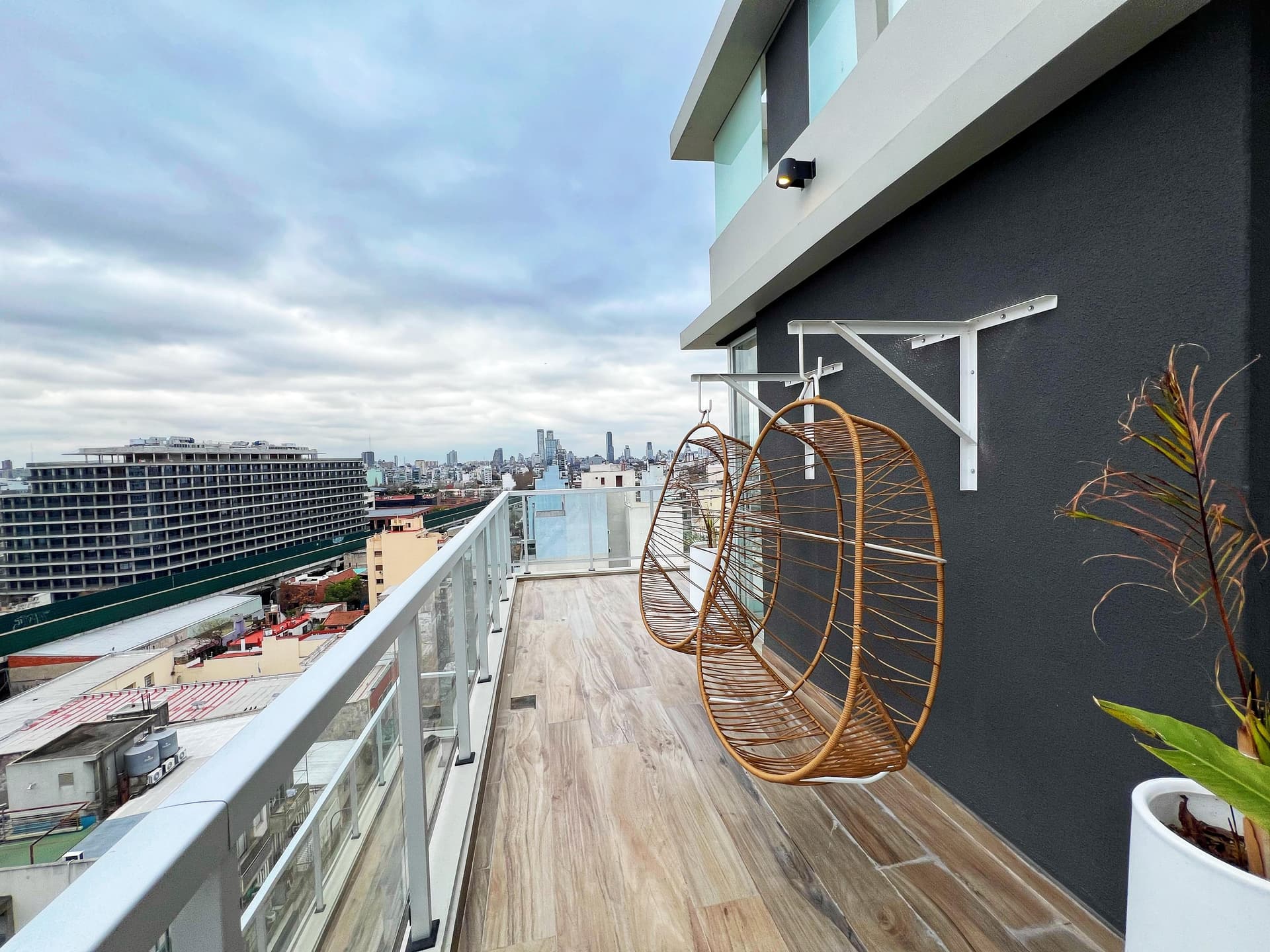 Terraza del edificio con dos sillas colgantes de mimbre y baranda de vidrio.