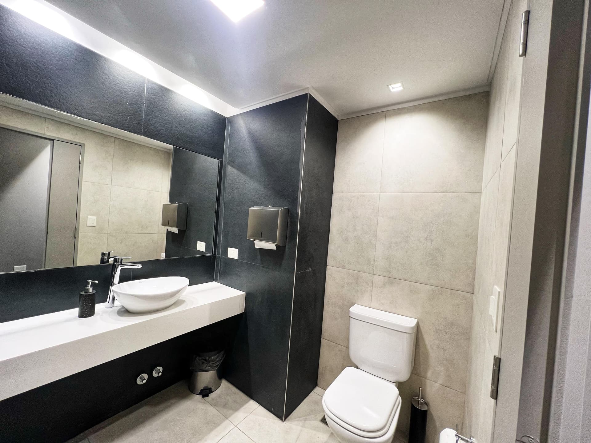Toilette del SUM con inodoro, lavatorio moderno y espejo amplio sobre la mesada.