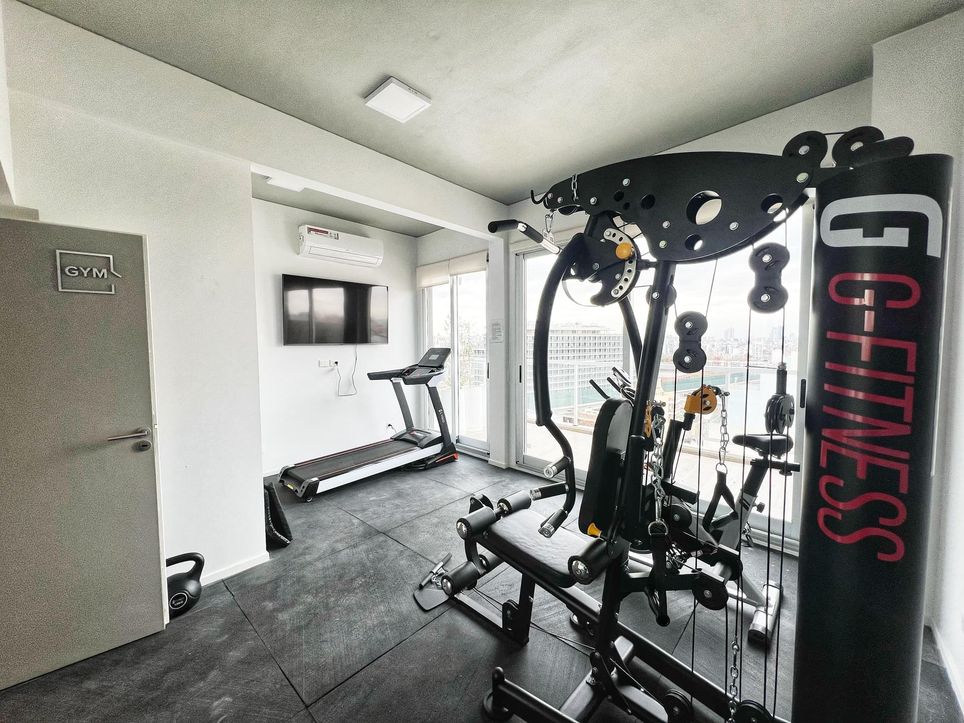 Gimnasio del edificio con máquina de entrenamiento multifuncional, cinta de correr y televisor.