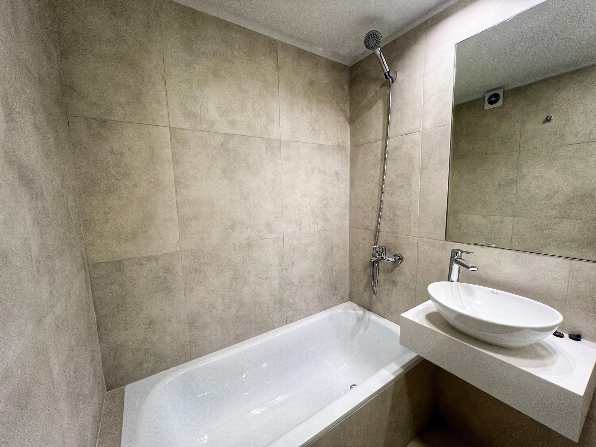 Baño completo con bañera, ducha de mano, vanitory blanco con bacha redonda y espejo.
