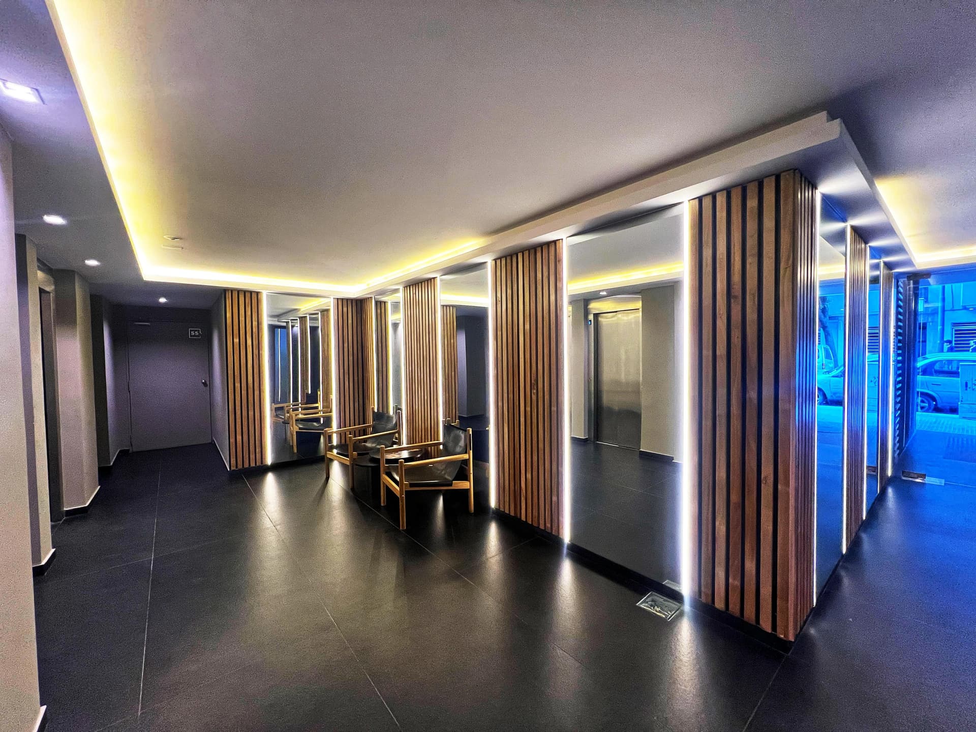 Pasillo de entrada del edificio moderno con espejos, paneles de madera iluminados y ascensores.