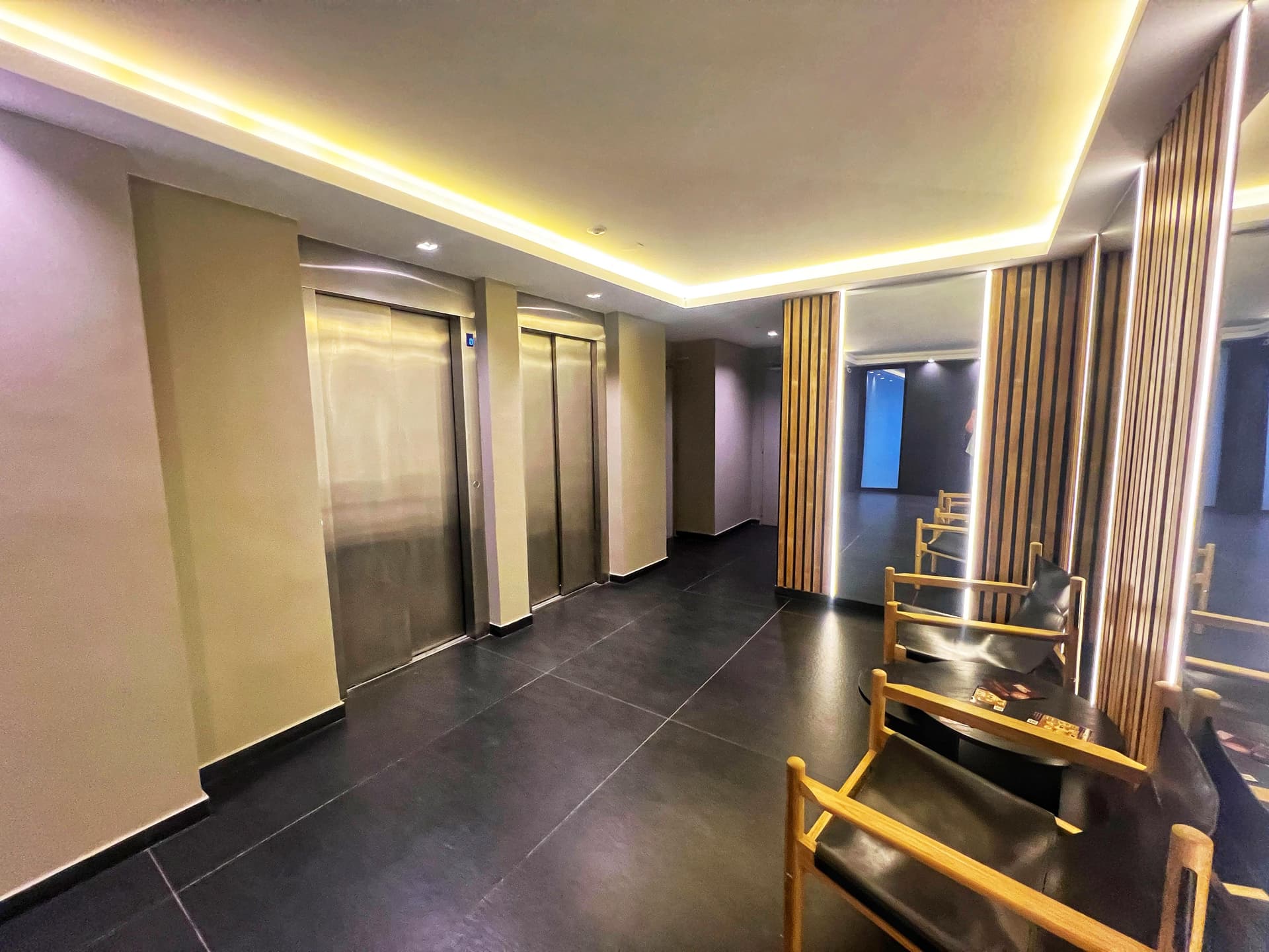 Pasillo de entrada del edificio con dos ascensores, sillones y decoración moderna.