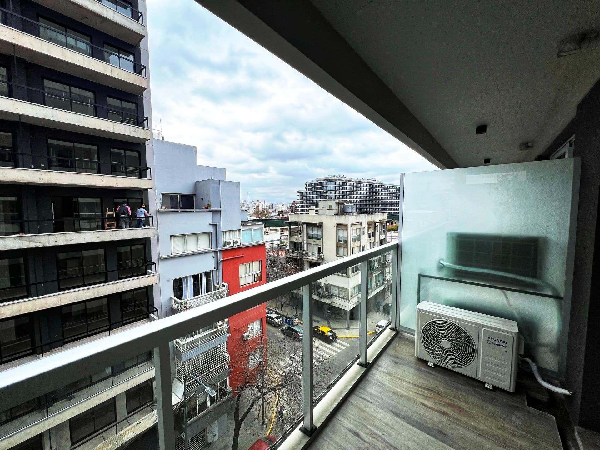 Balcón del departamento con unidad de aire acondicionado y vista a edificios de la ciudad.