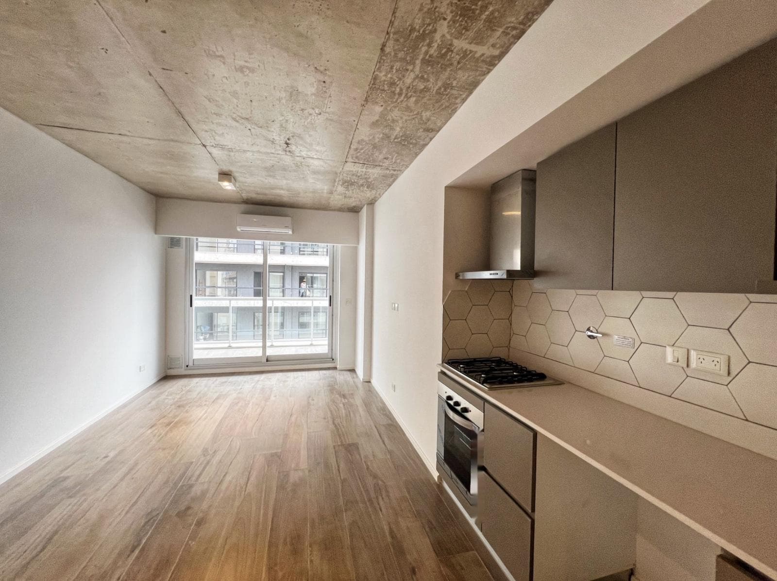 Living del departamento, ambiente vacío con cocina integrada y salida al balcón.