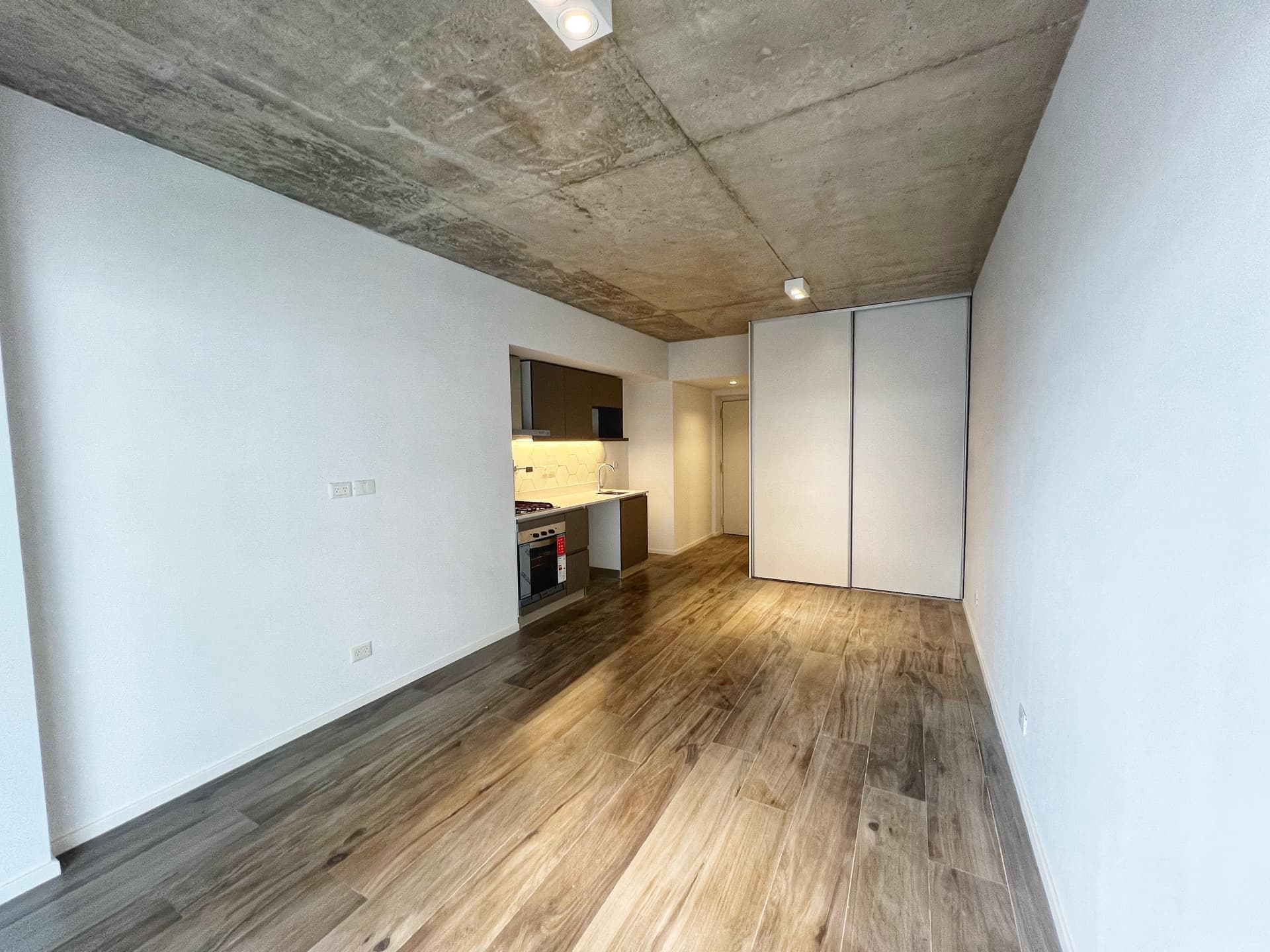 Living de departamento, ambiente vacío con cocina integrada, placard y piso de madera.