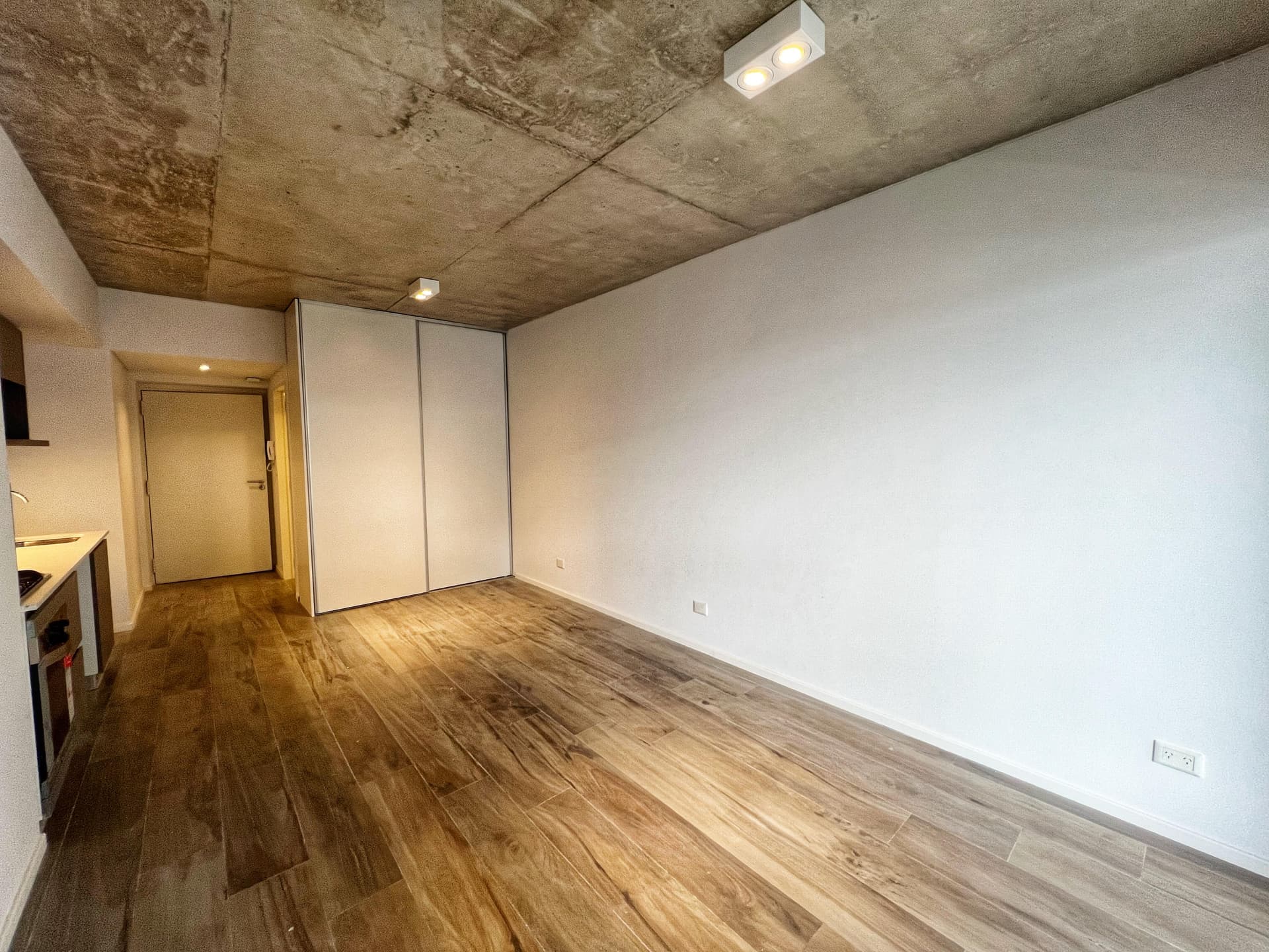 Living de departamento, ambiente vacío con placard, puerta y piso de madera.
