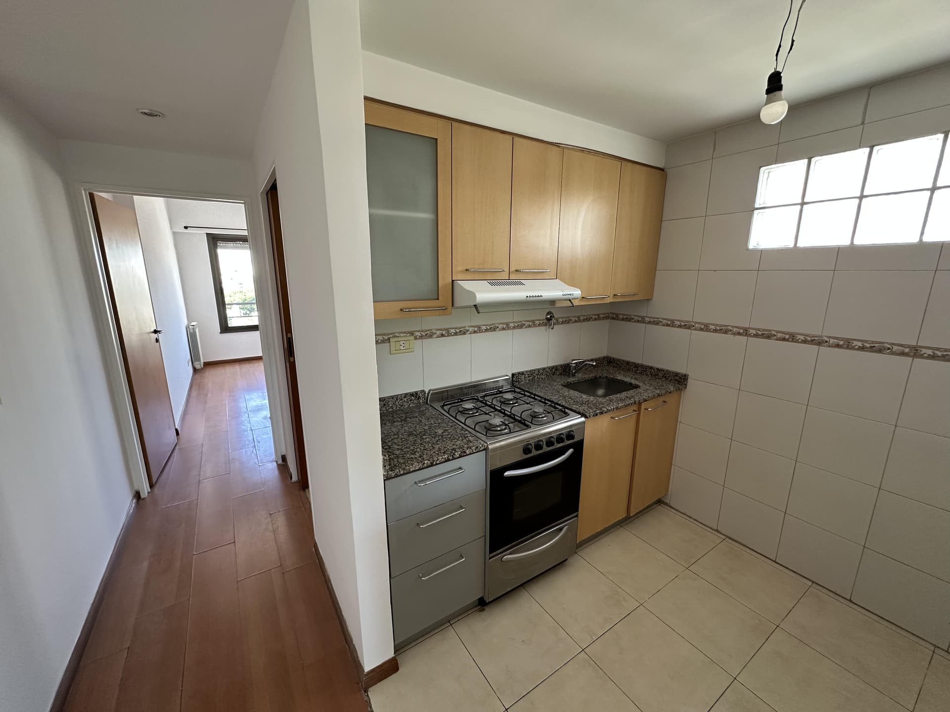 Cocina con anafe/horno, bacha y alacenas, conectada a pasillo.
