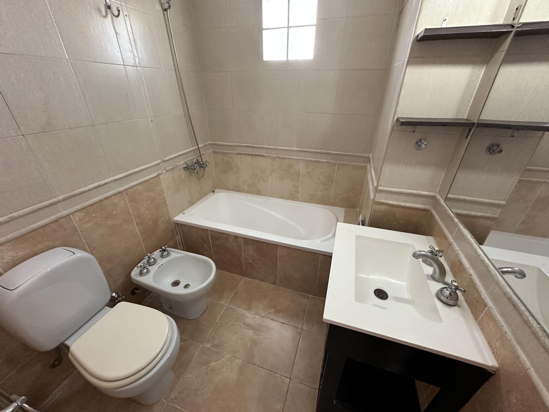 Baño completo con bañera, inodoro, bidet y vanitory, azulejos claros.