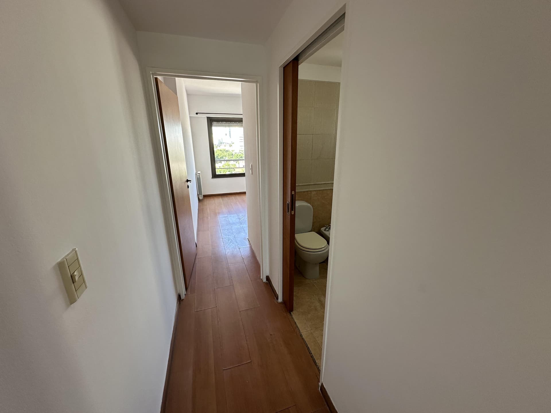 Pasillo con piso de madera que conecta baño y dormitorio.