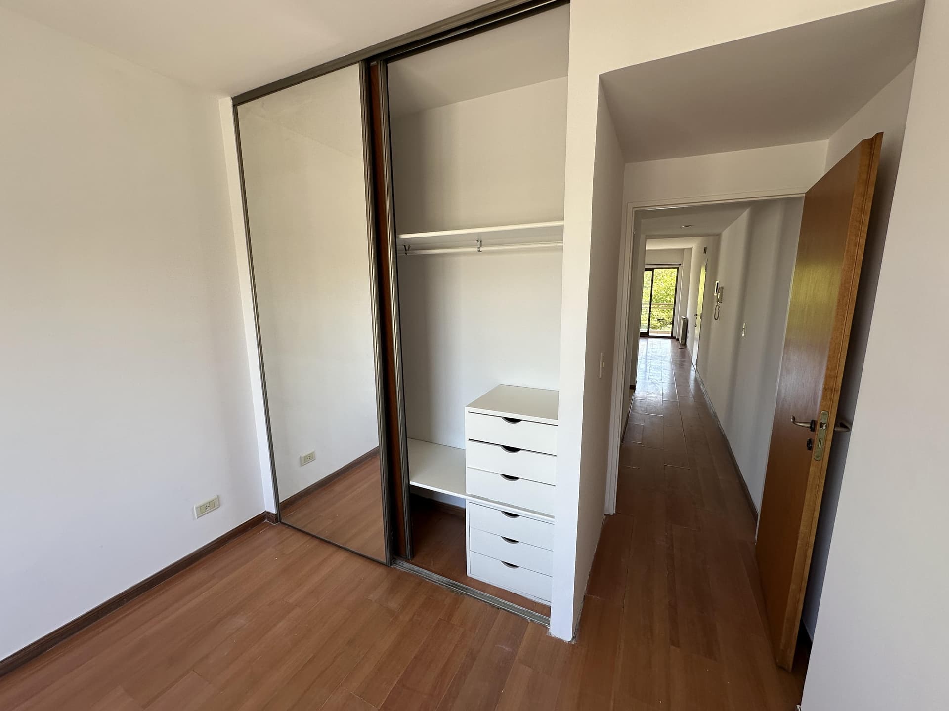 Dormitorio vacío con placard de puertas espejadas y piso de madera.