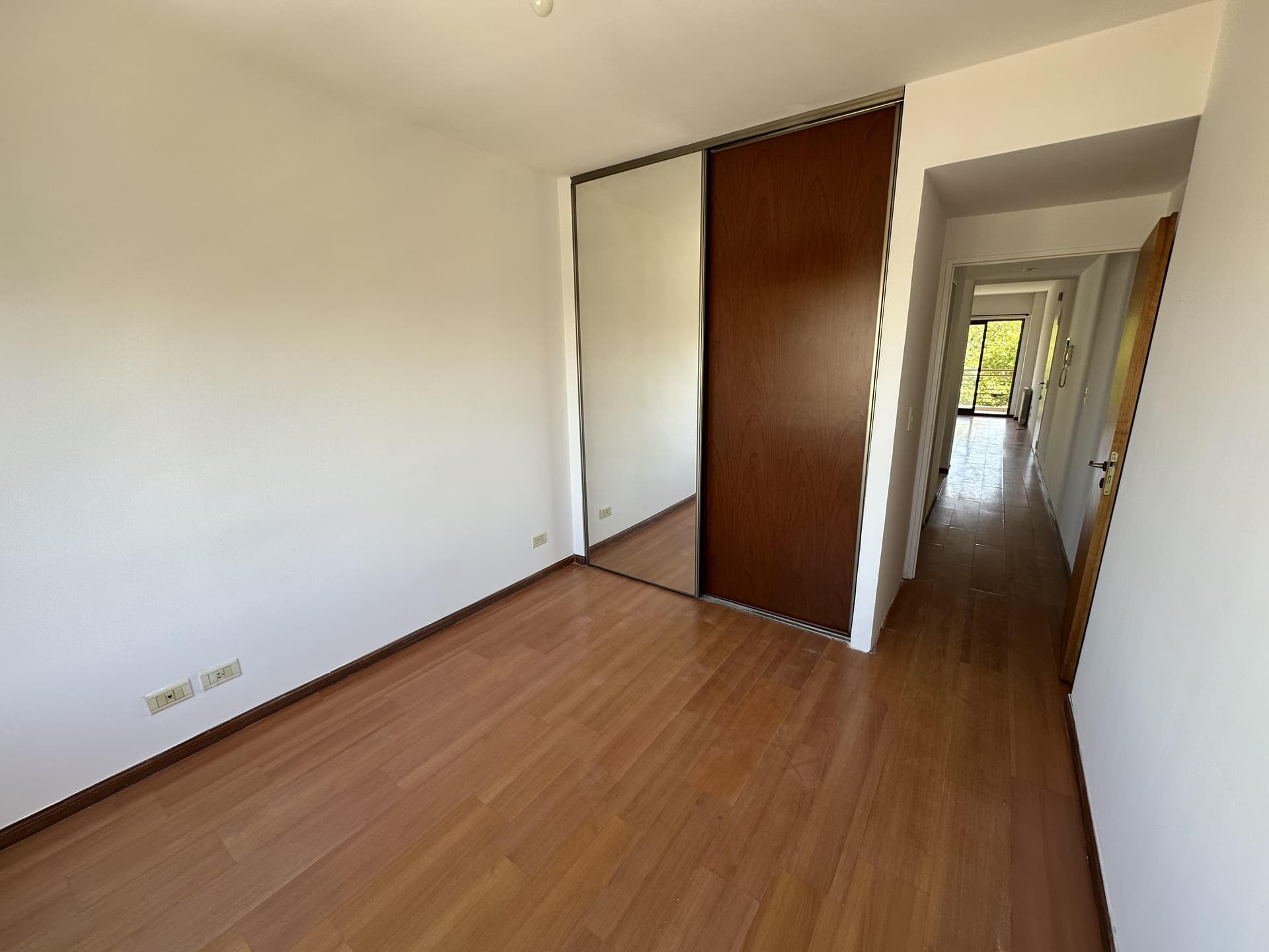 Dormitorio vacío con placard de madera y espejo, piso de madera.