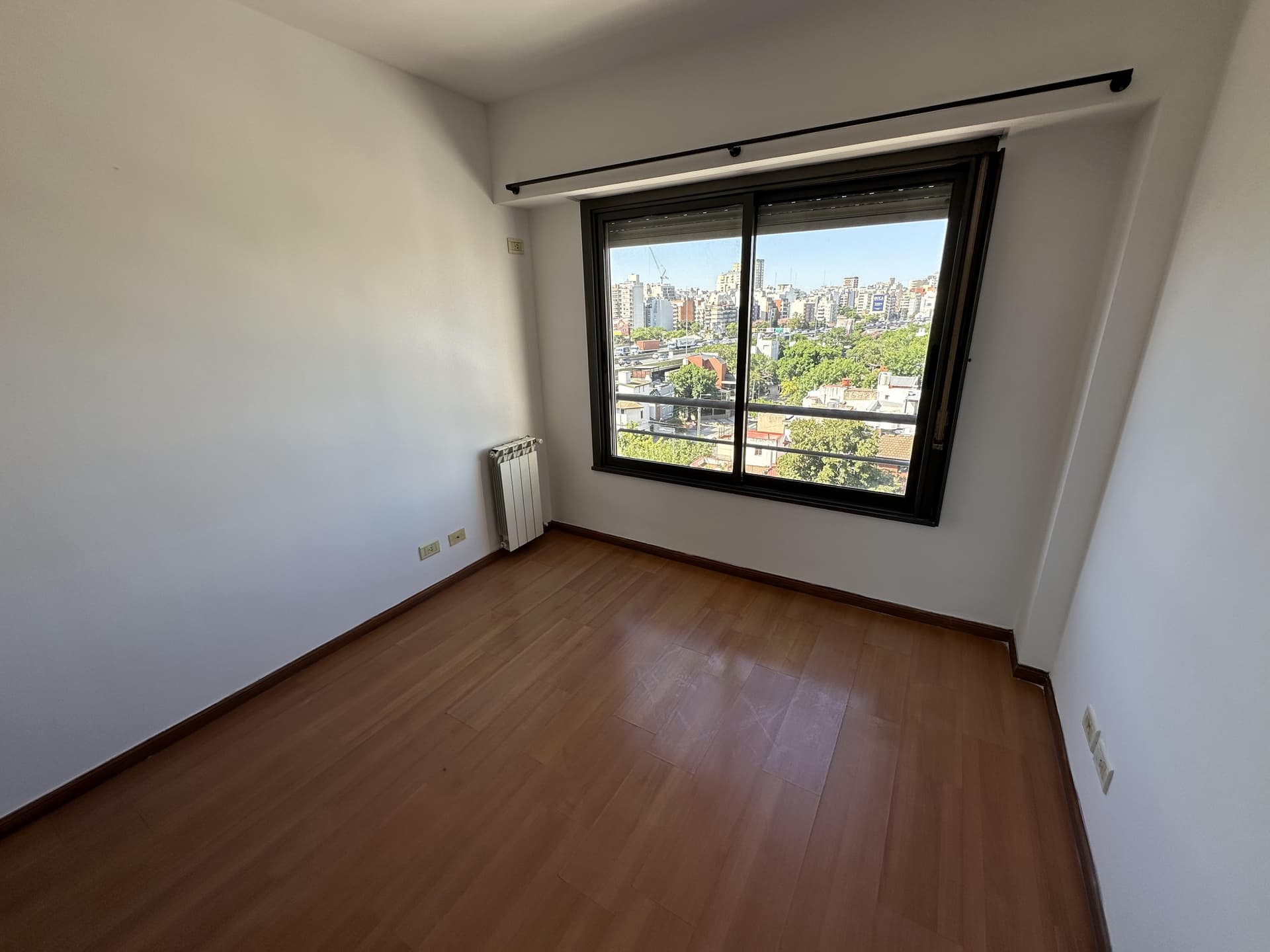 Dormitorio vacío con ventana con vista a la ciudad y radiador.