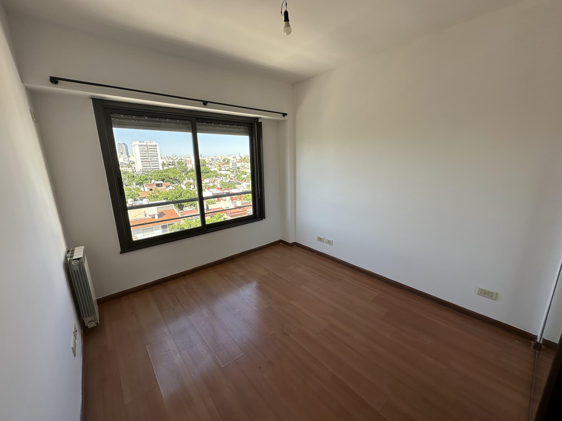 Dormitorio vacío con ventana grande con vista a la ciudad.